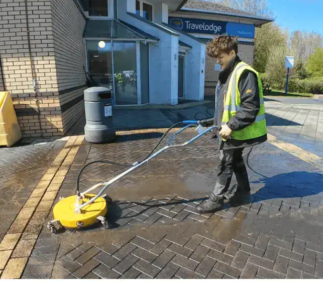 A cleaner using pressure washing on a brick pavement.