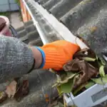 Alt: Close-up of a hand removing leaves from a gutter during exterior cleaning process.