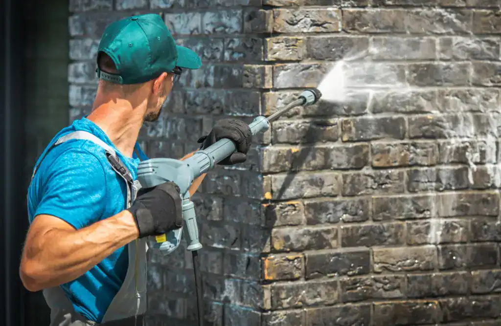 Man pressure washing exterior brickwork for deep clean.