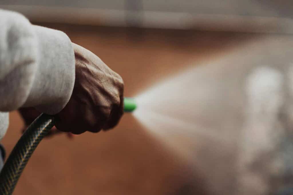 Close-up of a hand using a pressure washer to clean an exterior surface.