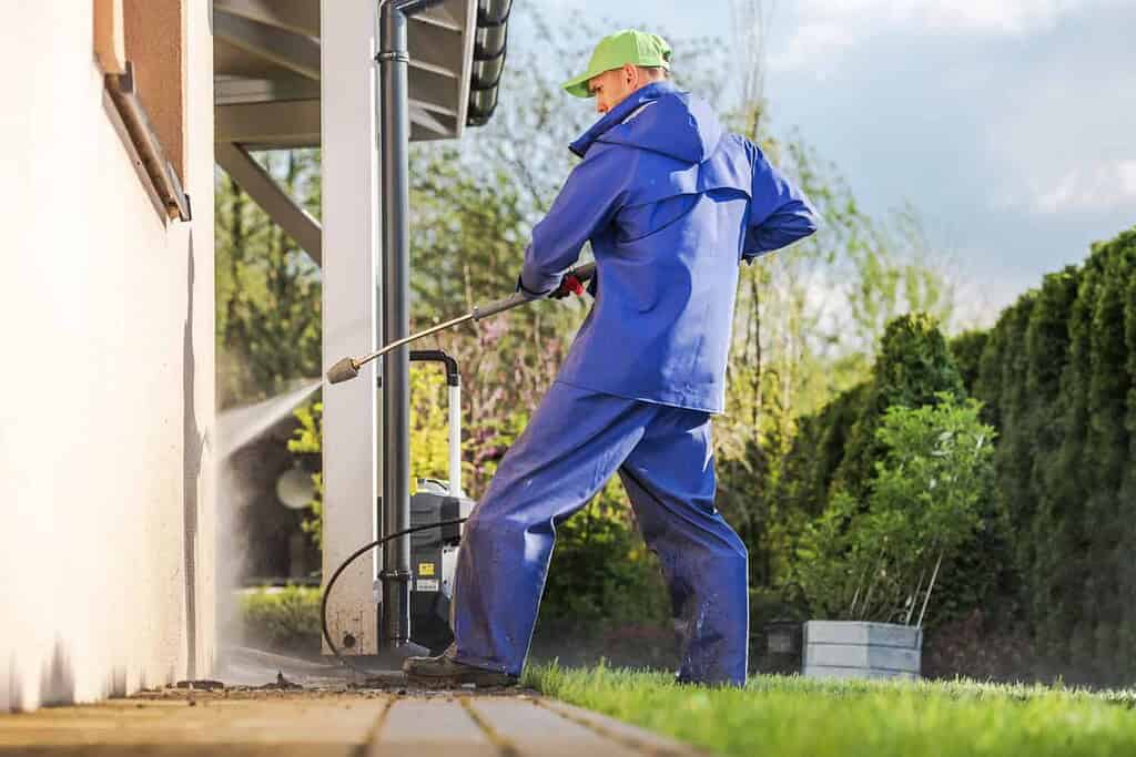 Pressure washing exterior of house with professional equipment.